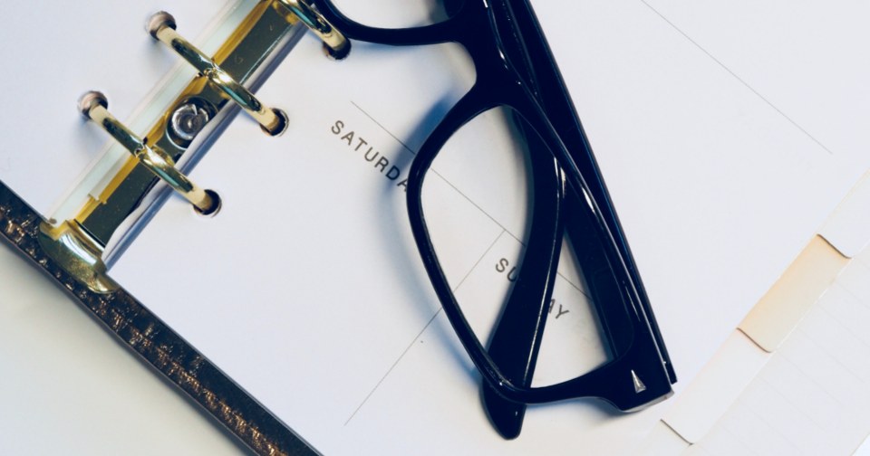 How to Plan a Monthly Email Content Calendar Black glasses resting on an open weekly planner page with ring binder
