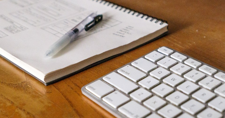 Email Marketing Terms Every Beginner Should Know Open notebook with a pen beside a white keyboard on a wooden desk